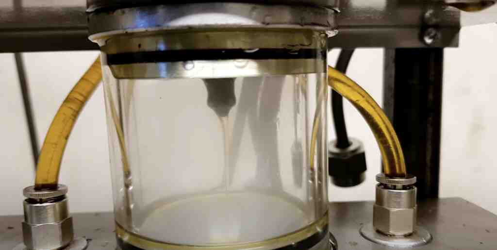 Injector on a test bench with fuel spray inside a glass measuring cylinder