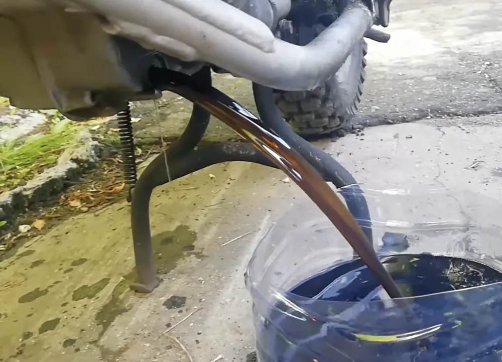 Brązowy, półprzejrzysty olej spływający z silnika motocykla podczas spuszczania