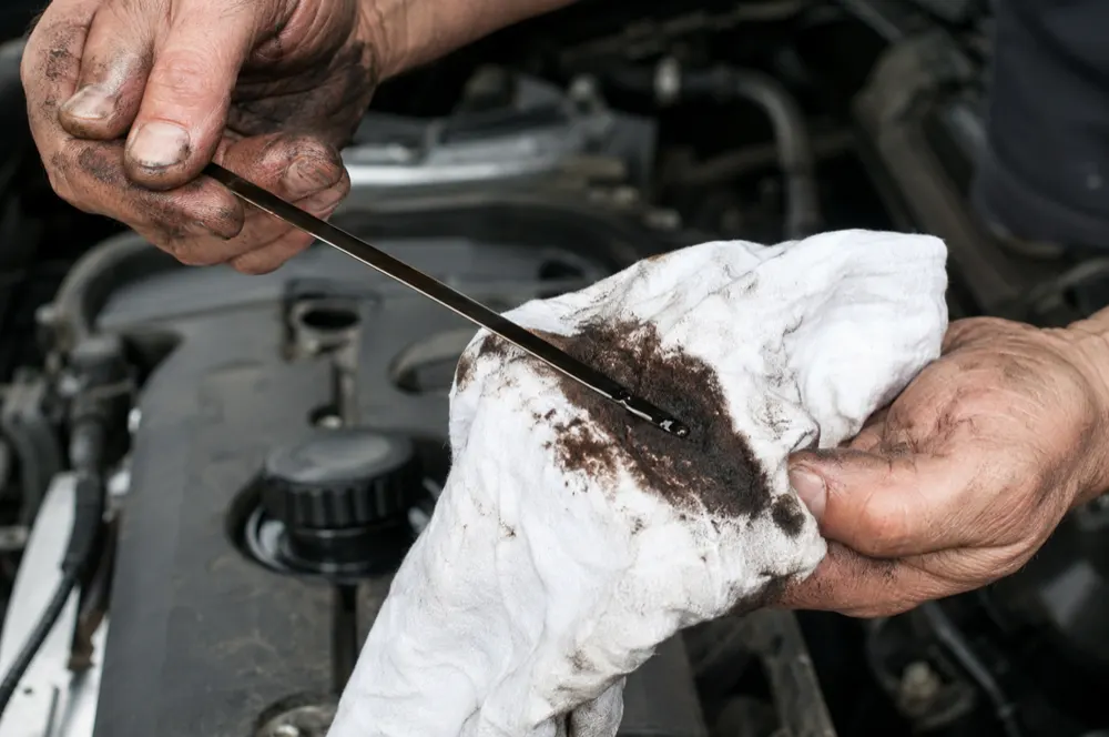 Dipstick with dark oil being wiped on a white rag over the engine bay