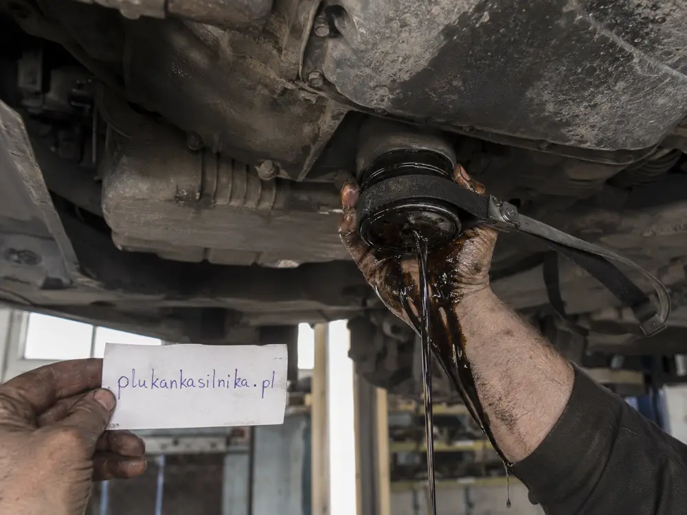 Mechanic unscrewing an oil filter with a strap wrench, black oil running over his hand