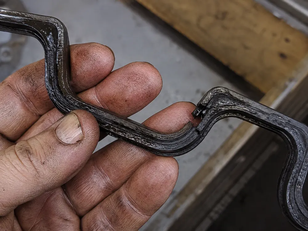 Old hardened valve cover gasket with a torn corner in a mechanic hand